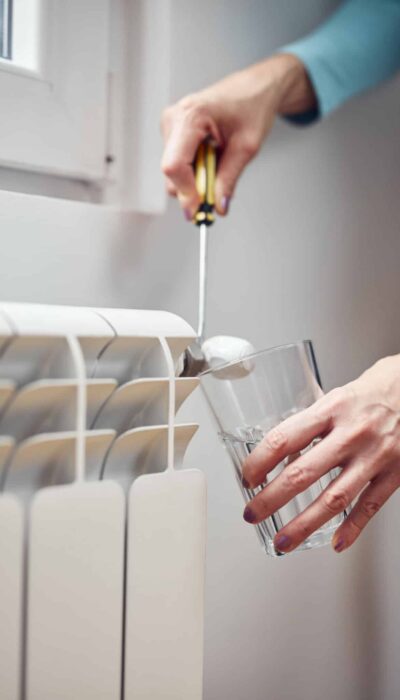 Woman fixing and bleeding air from central heating gas radiator system at home.