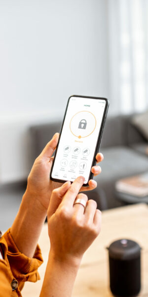 Young woman holding smart phone with launched security application at home. Concept of controlling and managing home security from a mobile device