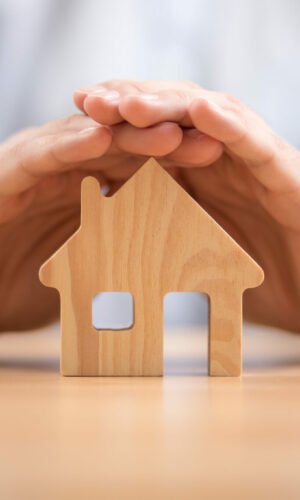 Wooden toy house protected by hands. Home insurance concept