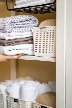 Domestic woman in pajamas neatly putting folded linens into cupboard vertical storage system use Marie Kondo method. Female housewife spring seasonal cleaning space organizer with organized boxes