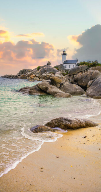 The Pontusval lighthouse, located on a rocky point in northern Finistere in Brittany, overlooks a sea of transparent turquoise waters during sunrise.