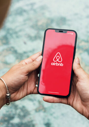 Girl in the park holding a smartphone with Airbnb app on the screen. Green area and an artificial lake. Rio de Janeiro, RJ, Brazil. February 2022.